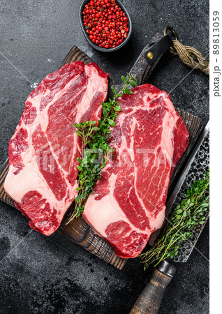 Raw chuck eye roll steaks premium beef meat on a cutting board. Black background. Top view 89813059