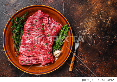 Raw beef skirt meat steak on a rustic plate with herbs. Dark background. Top view. Copy space 89813092