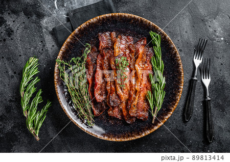 Hot Fried crunchy Bacon sizzling slices in plate with herbs. Black background. Top view Hot Fried crunchy Bacon sizzling slices in plate with herbs. Black background. Top view 89813414