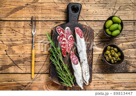 Spanish tapas Fuet Salami sausage slices with olives and rosemary on a wooden board. wooden background. Top view Spanish tapas Fuet Salami sausage slices with olives and rosemary on a wooden board. wooden background. Top view 89813447