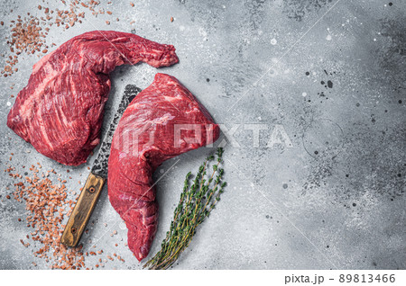 Unccoked tri-tip triangle roast, raw bottom sirloin steak on buther table with meat cleaver. Gray background. Top view. Copy space Unccoked tri-tip triangle roast, raw bottom sirloin steak on buther table with meat cleaver. Gray background. Top view. Copy space 89813466