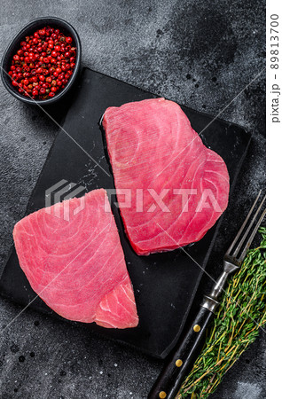 Raw tuna steak on a marble cutting Board . Black background. Top view Raw tuna steak on a marble cutting Board . Black background. Top view 89813700
