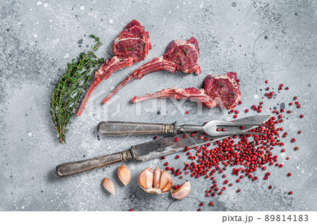 Uncooked lamb meat chops steaks on a butcher table with pepper and thyme. Gray background. Top view Uncooked lamb meat chops steaks on a butcher table with pepper and thyme. Gray background. Top view 89814183