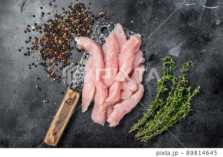 Slices of raw poultry meat on a butcher board with meat cleaver, chicken breast. Black background. Top view Slices of raw poultry meat on a butcher board with meat cleaver, chicken breast. Black background. Top view 89814645