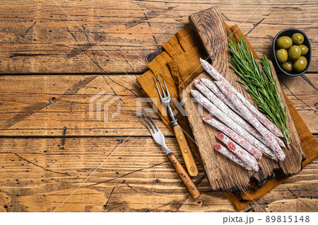 Spanish dry salami sausage Fuet with rosemary on wooden cutting board. Wooden background. Top view. Copy space Spanish dry salami sausage Fuet with rosemary on wooden cutting board. Wooden background. Top view. Copy space 89815148