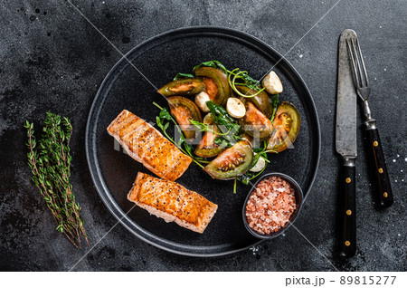 Fish meal with Roasted Salmon Fillet Steaks and arugula tomato salad on a plate. Black background. Top view 89815277