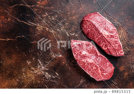 Raw Top Blade or flat iron beef meat steaks on a butcher table. Dark background. Top View. Copy space Raw Top Blade or flat iron beef meat steaks on a butcher table. Dark background. Top View. Copy space 89815315