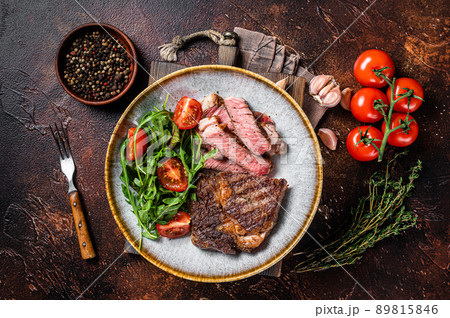 BBQ Grilled rib eye steak, fried rib-eye beef meat on a plate with green salad. Dark background. top view 89815846