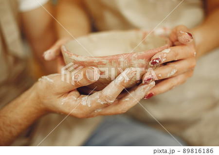 Mutual creative work. Young beautiful couple in casual clothes and aprons. People creating a bowl on a pottery wheel in a clay studio. Mutual creative work. Young beautiful couple in casual clothes and aprons. People creating a bowl on a pottery wheel in a clay studio. 89816186