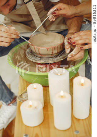 Mutual creative work. Young beautiful couple in casual clothes and aprons. People creating a bowl on a pottery wheel in a clay studio. Mutual creative work. Young beautiful couple in casual clothes and aprons. People creating a bowl on a pottery wheel in a clay studio. 89816211