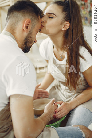 Mutual creative work. Young beautiful couple in casual clothes and aprons. People creating a bowl on a pottery wheel in a clay studio. 89816267