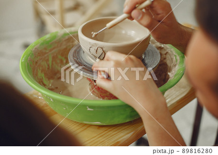 Mutual creative work. Young beautiful couple in casual clothes and aprons. People creating a bowl on a pottery wheel in a clay studio. 89816280
