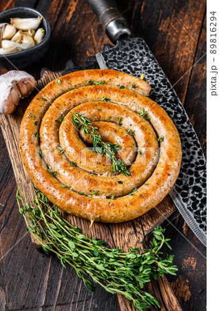 BBQ spiral sausage from pork and beef meat on a wooden cutting board. Dark wooden background. Top view 89816294