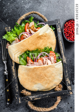 Doner kebab with grilled chicken meat and vegetables in pita bread on a wooden tray. Black background. Top view Doner kebab with grilled chicken meat and vegetables in pita bread on a wooden tray. Black background. Top view 89816539