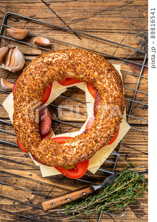 Bagel sandwich with lettuce, tomato, yellow cheese and sausages. Wooden background. Top view Bagel sandwich with lettuce, tomato, yellow cheese and sausages. Wooden background. Top view 89816541