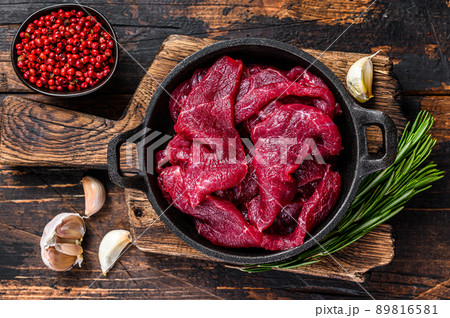 Fresh raw diced slices of red beef fiilet meat in cast iron pan. Dark wooden background. Top view Fresh raw diced slices of red beef fiilet meat in cast iron pan. Dark wooden background. Top view 89816581