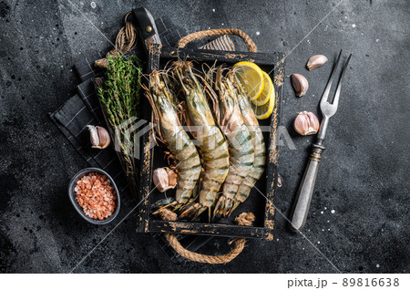 Raw fresh Giant Black tiger prawns shrimps in a tray with lemon and thyme. Black background. Top view Raw fresh Giant Black tiger prawns shrimps in a tray with lemon and thyme. Black background. Top view 89816638