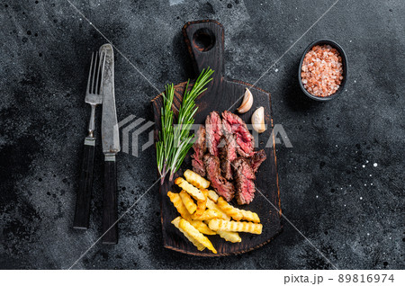 Roasted sliced machete skirt beef meat steak on wooden board with french fries. Black background. Top view 89816974