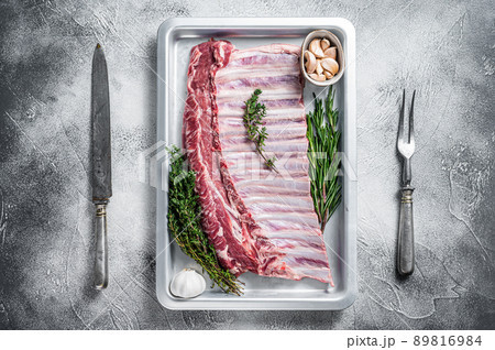Uncooked raw rack of lamb ribs in baking dish with herbs. White background. Top view Uncooked raw rack of lamb ribs in baking dish with herbs. White background. Top view 89816984