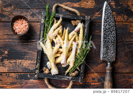 Raw Chicken paws feets on butcher chopping board with knife. Dark wooden background. Top view 89817207