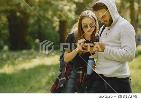 Tourists in a summer forest. Girl in a black t-shirt. Man use a phone. 89817249