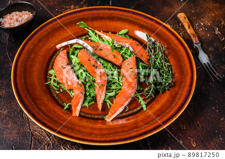 Salad with arugula and smoked salmon fillet slices. Dark background. Top view 89817250