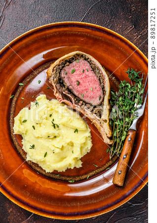 Beef Wellington pastry with mushed potato on a rustic plate. Dark background. Top view 89817251