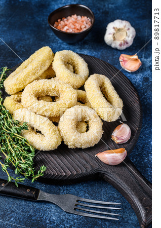 Frozen raw onion rings in breadcrumbs on a cutting board. Dark blue background. Top view Frozen raw onion rings in breadcrumbs on a cutting board. Dark blue background. Top view 89817713
