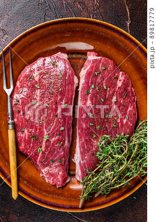 Raw rump cap steak or top sirloin steak in rustic plate with thyme and olive oil. Dark background. Top view 89817779