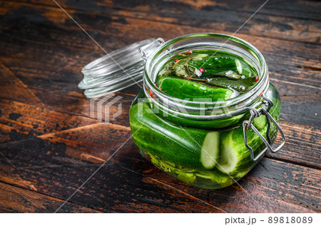 Green salted cucumbers in a glass jar. Canned vegetables. Dark Wooden background. Top view. 89818089