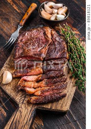 Roasted and sliced rib eye beef meat steak on a wooden cutting board with thyme. Dark wooden background. Top view Roasted and sliced rib eye beef meat steak on a wooden cutting board with thyme. Dark wooden background. Top view 89818121