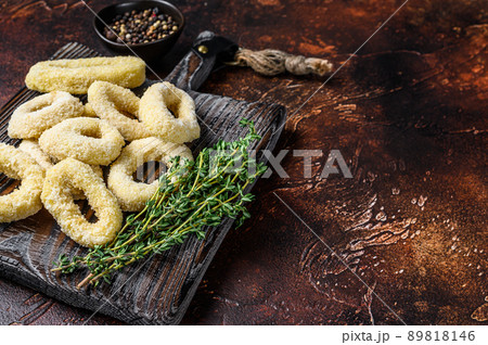 Frozen raw squid rings in breadcrumbs on a cutting board. Dark background. Top view. Copy space 89818146