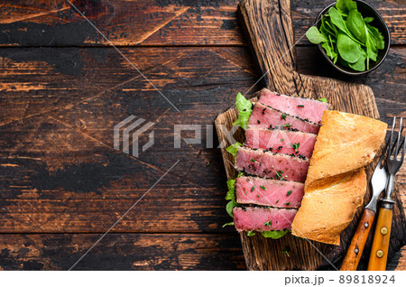 Grilled Ahi Tuna Steak and Avocado Sandwich with arugula on a cutting board. Dark wooden background. Top view. Copy space 89818924