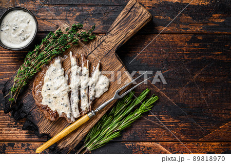 Roast fillet beef meat steak with peppercorn sauce on wooden board. Dark wooden background. Top view. Copy space 89818970