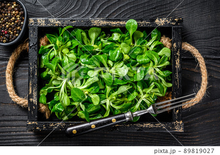 Fresh green lambs lettuce salad leaves on a wooden tray. Black wooden background. Top view Fresh green lambs lettuce salad leaves on a wooden tray. Black wooden background. Top view 89819027