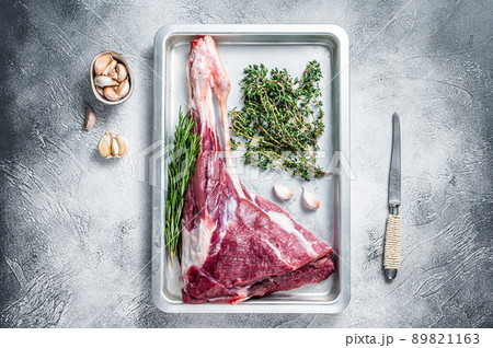 Uncooked Raw goat or lamb leg with herbs in baking tray. White background. Top view Uncooked Raw goat or lamb leg with herbs in baking tray. White background. Top view 89821163