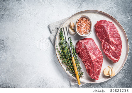Raw Oyster Top Blade or flat iron roast beef meat steaks on a plate with herbs. White background. Top View. Copy space Raw Oyster Top Blade or flat iron roast beef meat steaks on a plate with herbs. White background. Top View. Copy space 89821258