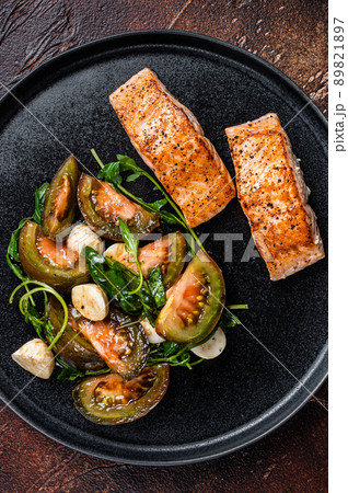 Grilled Salmon Fillet Steaks with arugula and tomato salad on a plate. Dark background. Top view 89821897