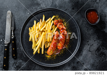 German currywurst Sausages with French fries on a plate. Black background. Top view German currywurst Sausages with French fries on a plate. Black background. Top view 89821921