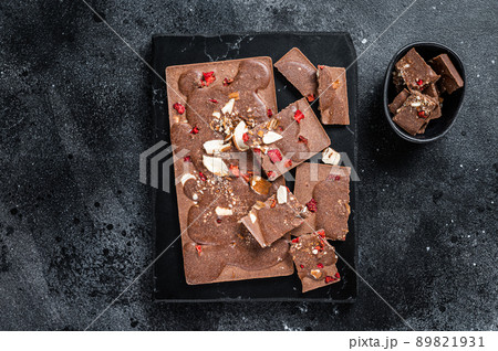 Craft homemade chocolate bars chopped on marble board. Black background. Top view 89821931