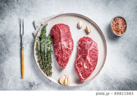 Raw Oyster Top Blade or flat iron roast beef meat steaks on a plate with herbs. White background. Top View 89821983