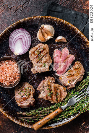 Barbecue Grilled lamb loin chops steaks, saddle in a plate with herbs. Dark background. Top view 89822024