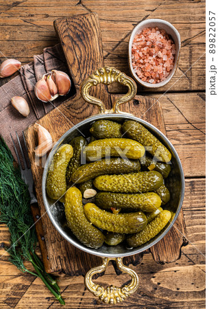 Pickled gherkins cucumbers in bowl with herbs. Wooden background. Top view Pickled gherkins cucumbers in bowl with herbs. Wooden background. Top view 89822057