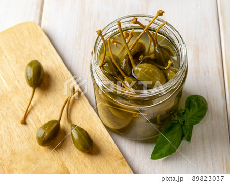 Marinated caper fruits in an open glass jar on a wooden table. Marinated caper fruits in an open glass jar on a wooden table. 89823037