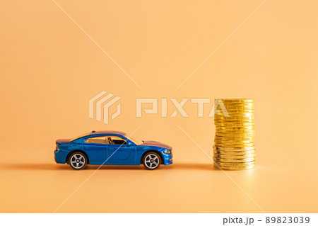 Blue car model and stack of golden coins against orange background. Blue car model and stack of golden coins against orange background. 89823039