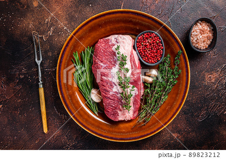 Raw round beef meat prime cut for roast on a rustic plate with herbs. Dark background. Top view Raw round beef meat prime cut for roast on a rustic plate with herbs. Dark background. Top view 89823212