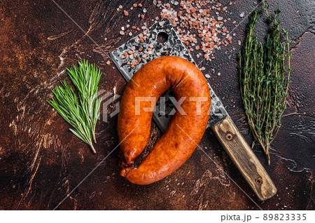 Hot Smoked sausage on a butcher rustic cleaver with herbs. Dark background. Top view Hot Smoked sausage on a butcher rustic cleaver with herbs. Dark background. Top view 89823335