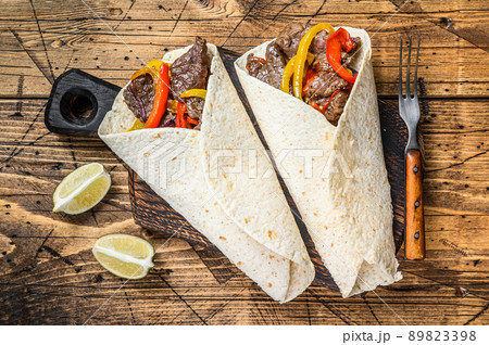 Fajitas Tortilla wrap with beef meat stripes, colored bell pepper and onions and salsa. Wooden background. Top view 89823398