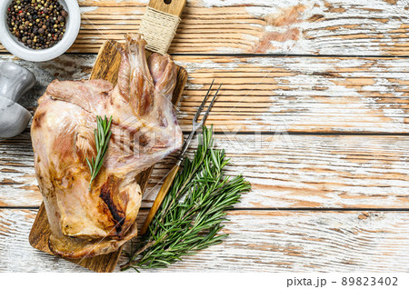 Oven Baked whole lamb shoulder on a cutting board. White wooden background. Top view. Copy space 89823402