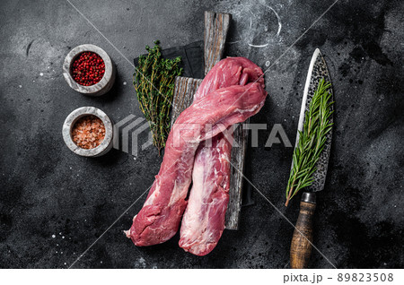 Tenderloin pork raw meat, uncooked fillet on wooden board with herbs. Black background. Top view 89823508
